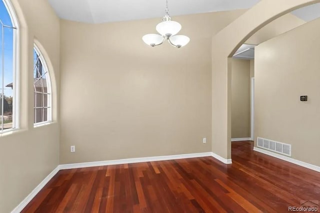 unfurnished room with arched walkways, wood finished floors, visible vents, and baseboards