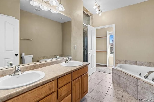 bathroom with vanity, tile patterned flooring, a relaxing tiled tub, and toilet