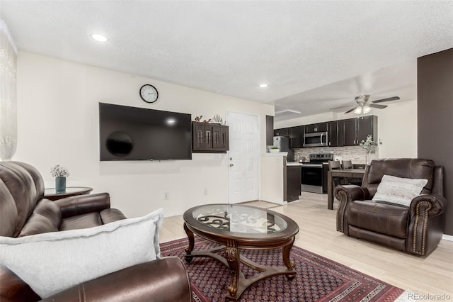 living room with a textured ceiling, light hardwood / wood-style floors, and ceiling fan