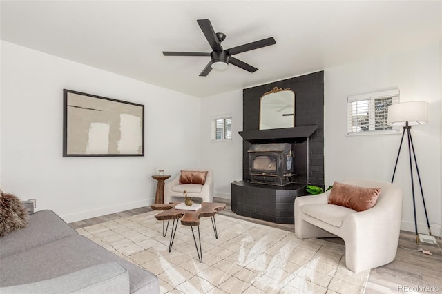 sitting room featuring a wood stove, light wood-style flooring, baseboards, and a ceiling fan