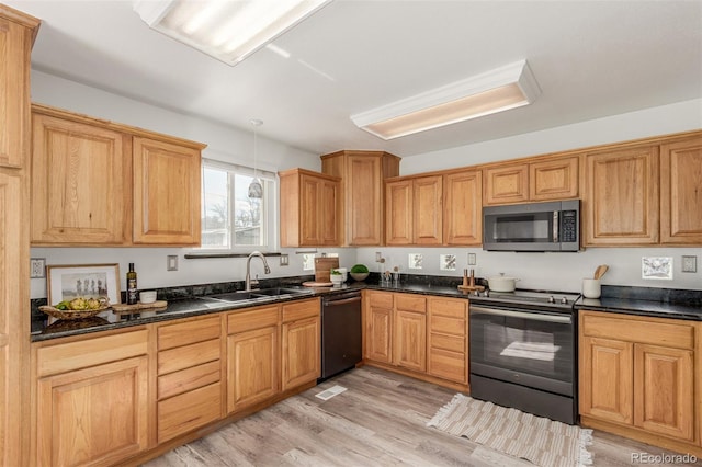 kitchen with a sink, appliances with stainless steel finishes, dark stone counters, light wood finished floors, and decorative light fixtures