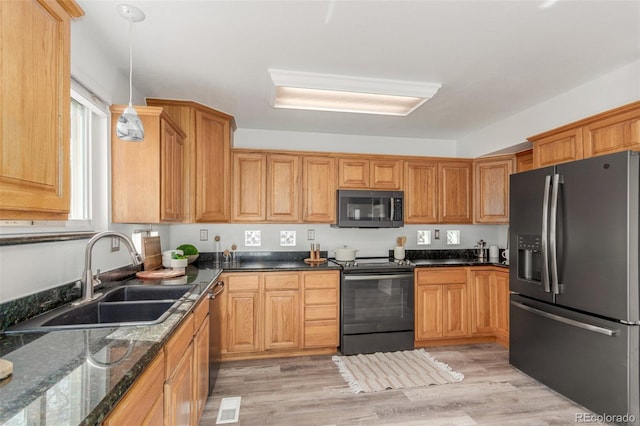 kitchen with appliances with stainless steel finishes, decorative light fixtures, a sink, and light wood-style flooring