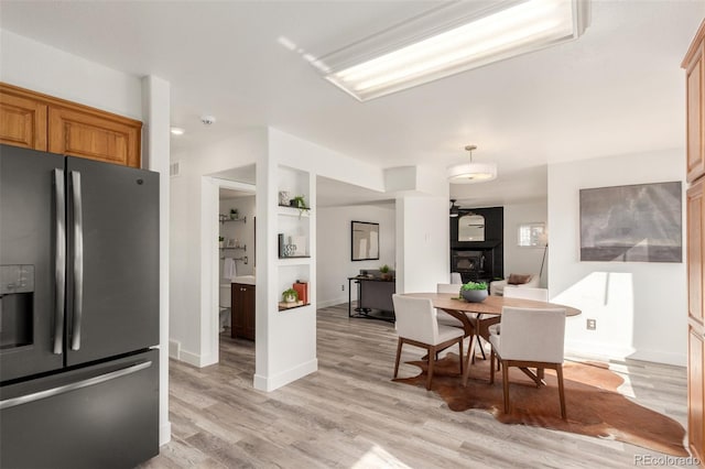 kitchen with a fireplace, stainless steel fridge, light wood-style flooring, and baseboards