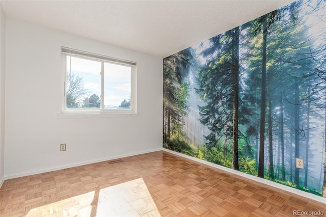 empty room featuring visible vents, a textured ceiling, and baseboards