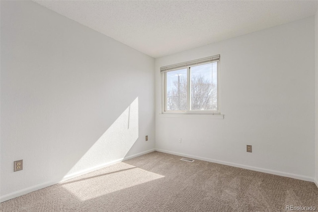 empty room featuring a textured ceiling, baseboards, visible vents, and light colored carpet