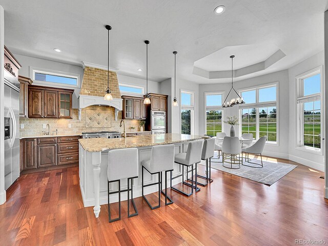 2131 Driver Ln, Erie, CO 80516 - kitchen featuring a tray ceiling, wall chimney range hood, dark wood-style floors, glass insert cabinets, and a kitchen breakfast bar