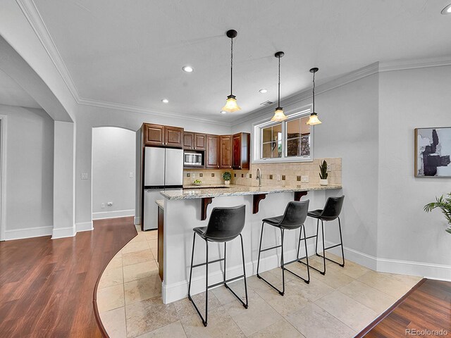 2131 Driver Ln, Erie, CO 80516 - kitchen with appliances with stainless steel finishes, a peninsula, a breakfast bar, arched walkways, and light stone countertops