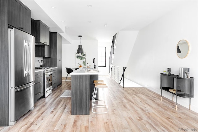 kitchen with a kitchen bar, a center island with sink, light hardwood / wood-style flooring, appliances with stainless steel finishes, and pendant lighting