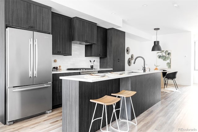 kitchen featuring hanging light fixtures, an island with sink, sink, and stainless steel fridge