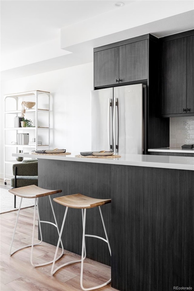 kitchen with stainless steel fridge, kitchen peninsula, light hardwood / wood-style floors, and backsplash