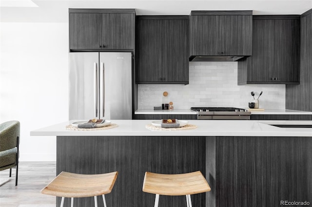 kitchen with stainless steel refrigerator, a kitchen bar, light hardwood / wood-style floors, and stove