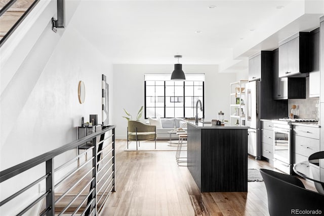 kitchen featuring a kitchen island, backsplash, hanging light fixtures, light hardwood / wood-style floors, and stainless steel appliances