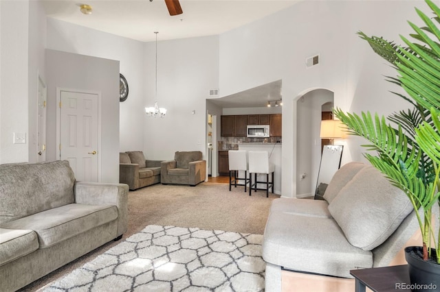 carpeted living room featuring high vaulted ceiling and ceiling fan with notable chandelier