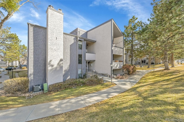 view of home's exterior with a yard, central AC unit, a chimney, and stucco siding