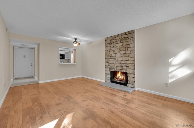 unfurnished living room featuring light wood finished floors, baseboards, ceiling fan, a textured ceiling, and a fireplace