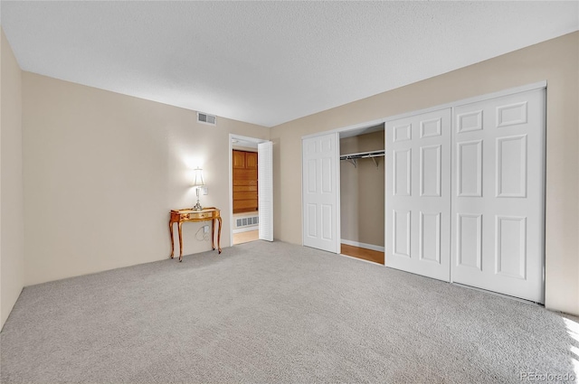 unfurnished bedroom with a textured ceiling, a closet, carpet, and visible vents