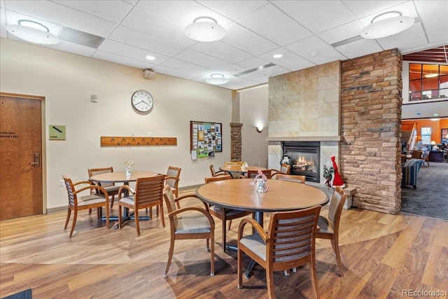 dining area featuring a drop ceiling, wood-type flooring, and a tile fireplace