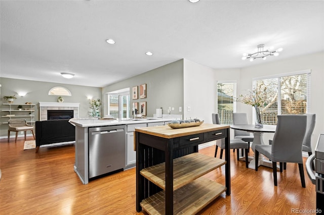 kitchen featuring sink, dishwasher, kitchen peninsula, a tiled fireplace, and light wood-type flooring