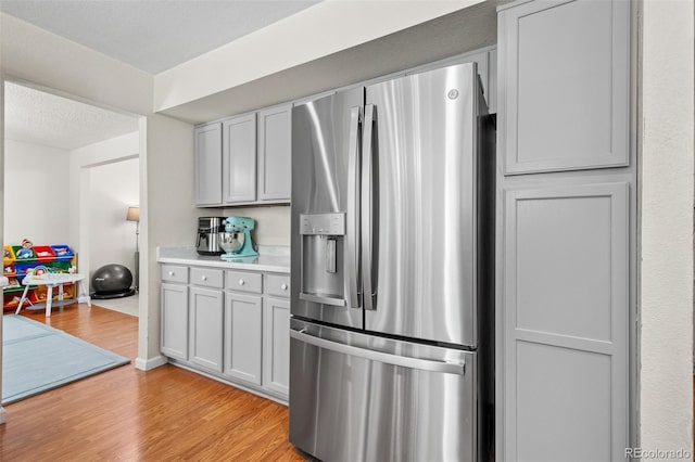 kitchen with stainless steel refrigerator with ice dispenser, light wood-type flooring, a textured ceiling, and gray cabinetry