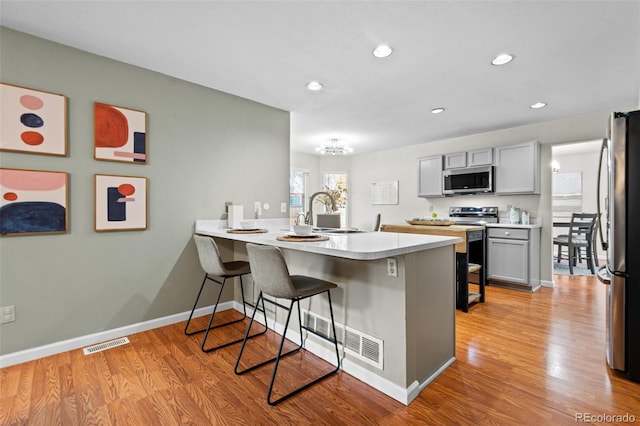 kitchen with kitchen peninsula, appliances with stainless steel finishes, light wood-type flooring, gray cabinetry, and a breakfast bar area