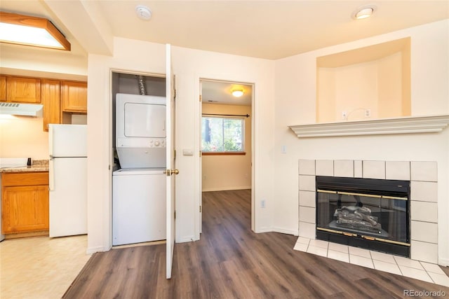 unfurnished living room with a tiled fireplace, wood-type flooring, and stacked washing maching and dryer