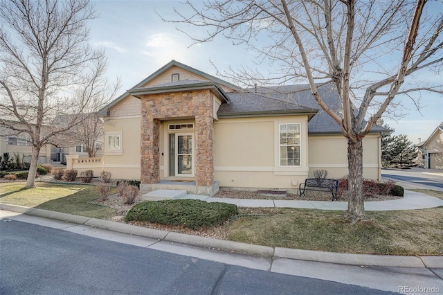 view of front of house featuring stone siding, roof with shingles, a front lawn, and stucco siding