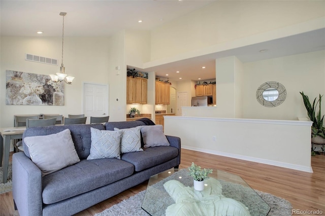 living room featuring baseboards, visible vents, a high ceiling, light wood-type flooring, and a chandelier