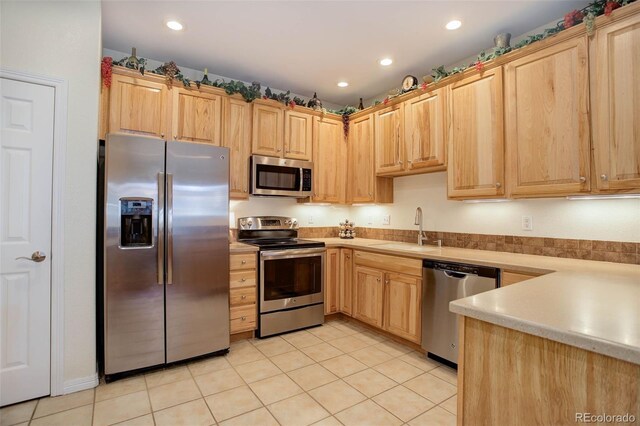 kitchen featuring recessed lighting, stainless steel appliances, a sink, light countertops, and light brown cabinetry