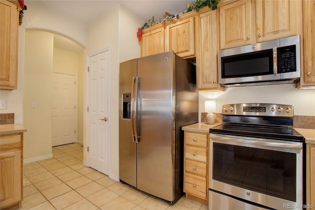 kitchen with arched walkways, light tile patterned floors, stainless steel appliances, light countertops, and light brown cabinetry