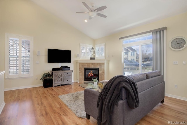 living area with a tile fireplace, a ceiling fan, baseboards, vaulted ceiling, and light wood-style floors