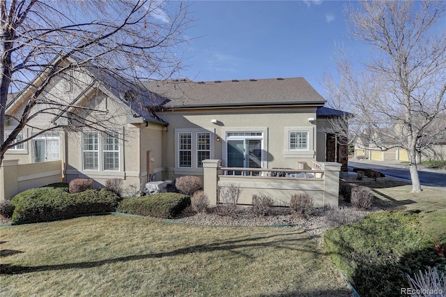 rear view of house featuring roof with shingles, a yard, and stucco siding