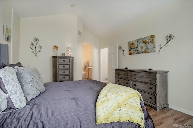 bedroom featuring arched walkways, visible vents, light wood-style flooring, vaulted ceiling, and baseboards