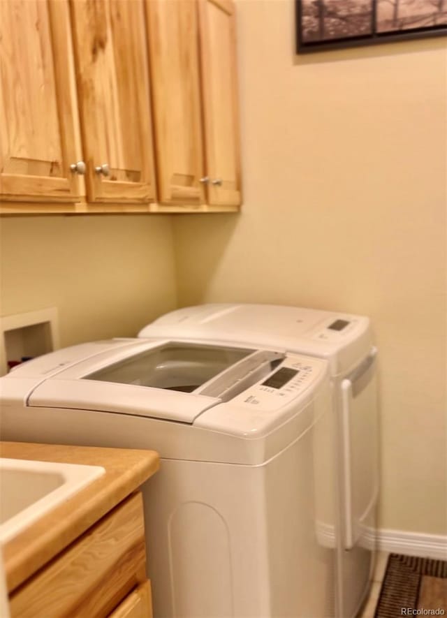 washroom featuring cabinet space, baseboards, and washer and clothes dryer