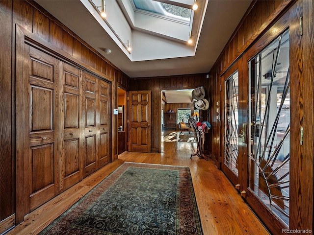 entrance foyer with a healthy amount of sunlight, wooden walls, a skylight, and light hardwood / wood-style flooring