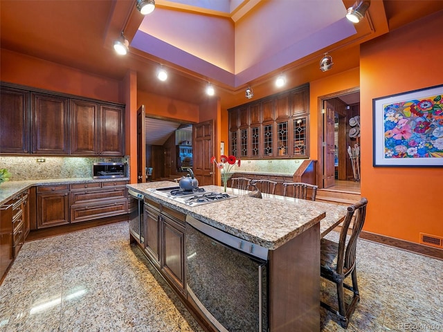 kitchen featuring a center island with sink, stainless steel appliances, a tray ceiling, backsplash, and a kitchen bar