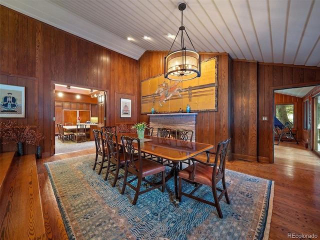 dining room with vaulted ceiling, a stone fireplace, and wooden walls