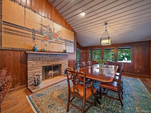 dining space with wood walls, a stone fireplace, light wood-type flooring, and lofted ceiling