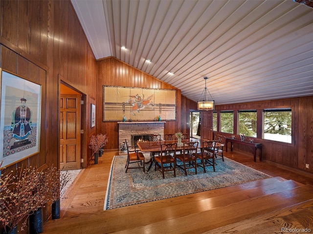 dining space featuring high vaulted ceiling, a stone fireplace, wooden walls, and light hardwood / wood-style floors