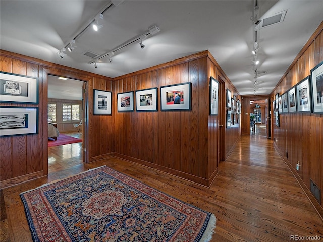 hall with wood walls, rail lighting, and dark hardwood / wood-style floors