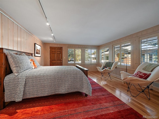 bedroom featuring wood-type flooring, wooden walls, and track lighting