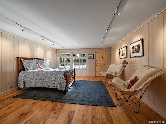 bedroom with hardwood / wood-style flooring, wooden walls, and rail lighting