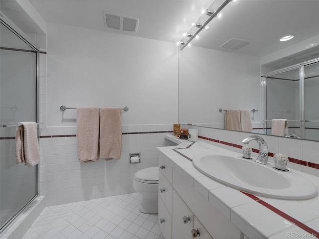 bathroom featuring tile flooring, vanity with extensive cabinet space, tile walls, walk in shower, and toilet