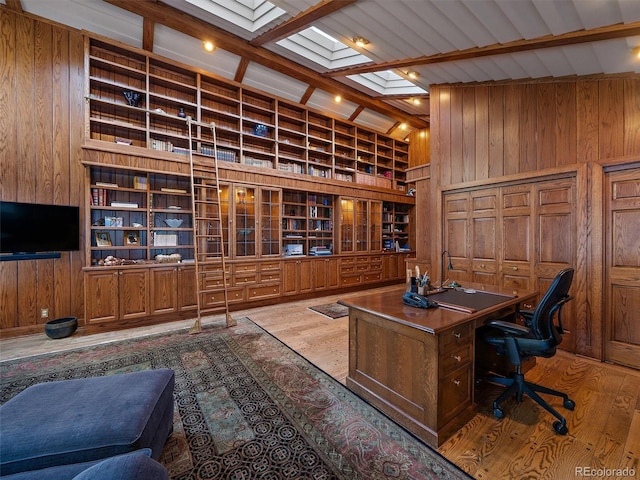 home office featuring a skylight, hardwood / wood-style flooring, beamed ceiling, built in shelves, and wooden walls