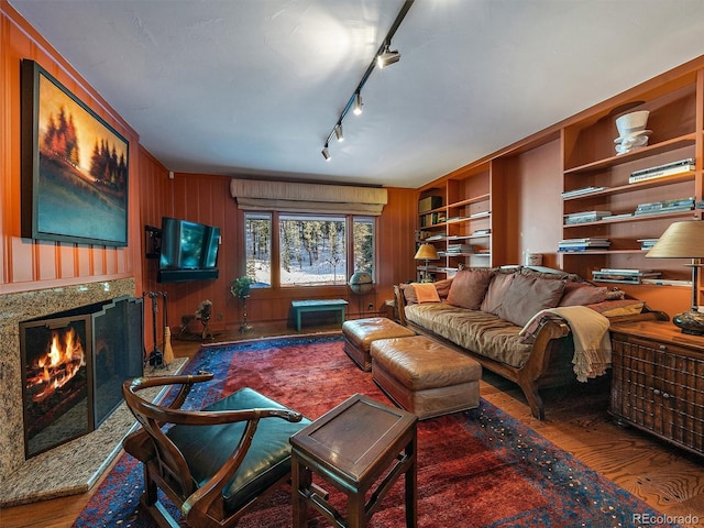 living room featuring a fireplace, wood walls, hardwood / wood-style flooring, track lighting, and built in shelves