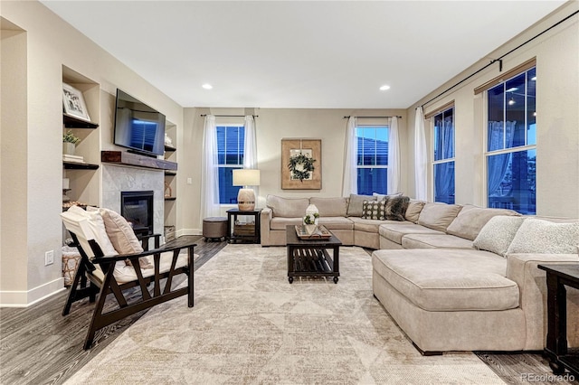 living area featuring a glass covered fireplace, wood finished floors, built in features, and baseboards