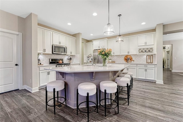 kitchen with a breakfast bar area, appliances with stainless steel finishes, light countertops, white cabinetry, and a sink