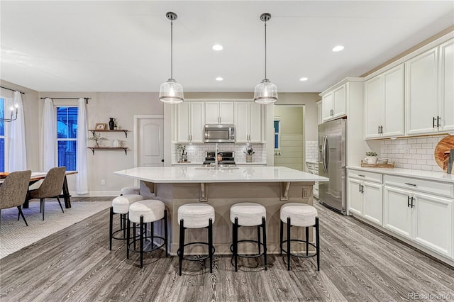 kitchen featuring wood finished floors, stainless steel appliances, light countertops, a kitchen bar, and white cabinetry