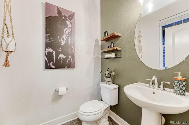 half bath with toilet, baseboards, a sink, and a textured wall