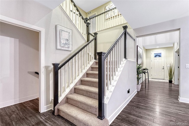 stairs with wood finished floors, a towering ceiling, and baseboards