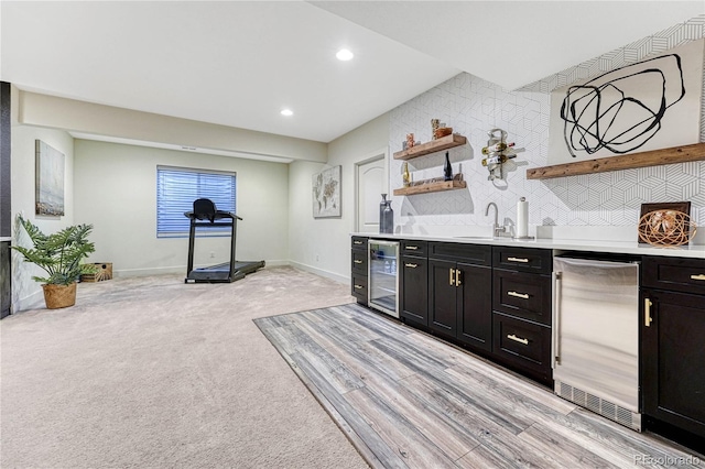 bar with indoor wet bar, light colored carpet, a sink, beverage cooler, and fridge